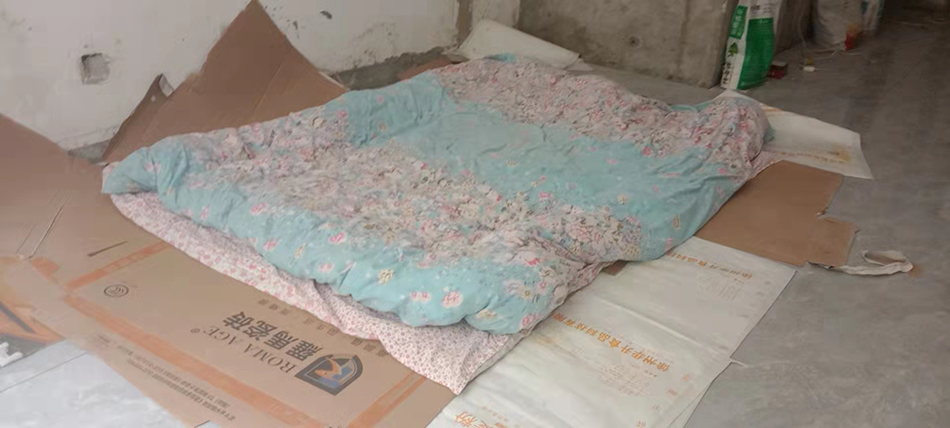 包裝瓷磚的紙板和家中帶來的被子，是何明中夫婦的床。